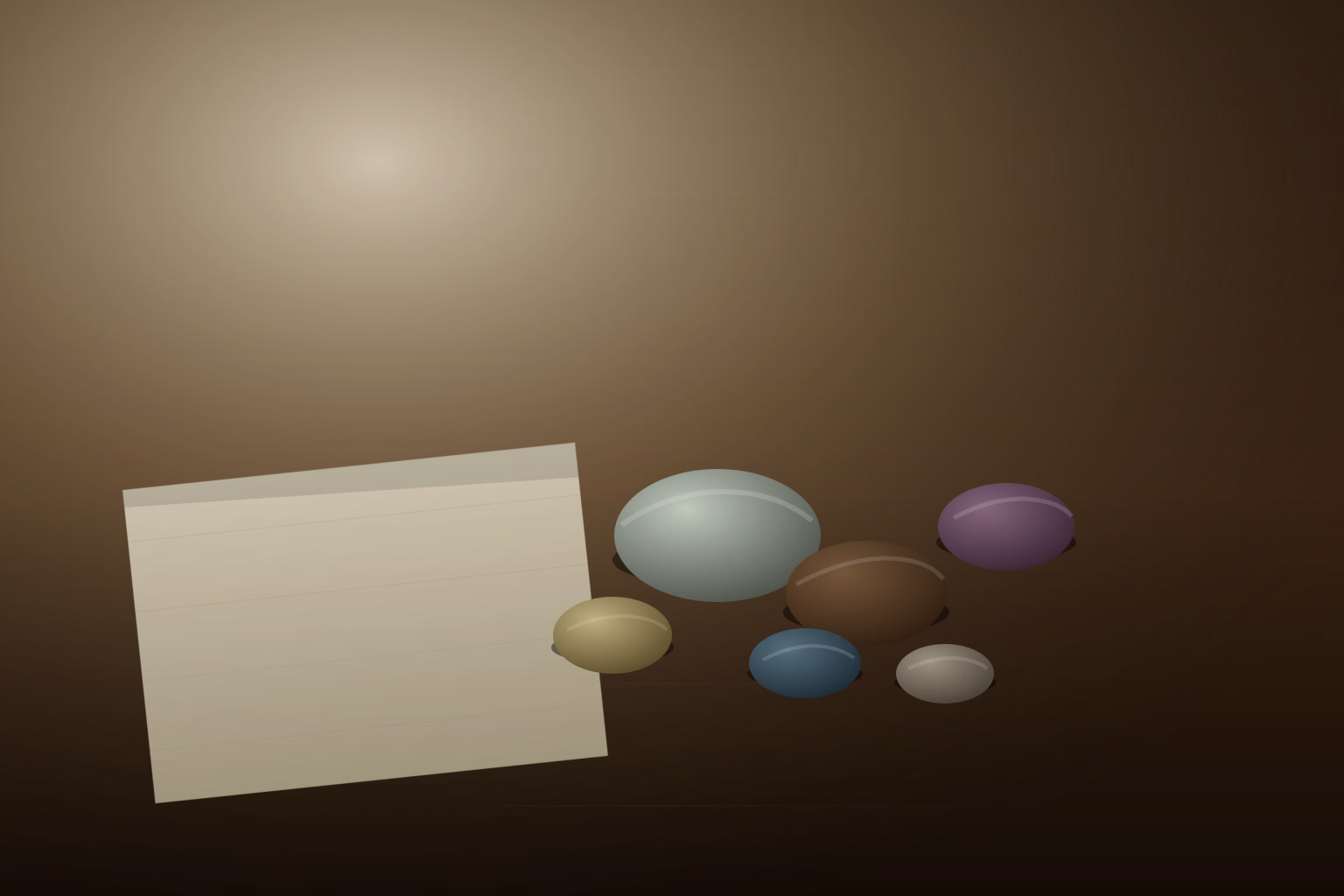 A small handful of coloured river stones arranged on a dark wooden table in soft morning light, beside a folded linen cloth.