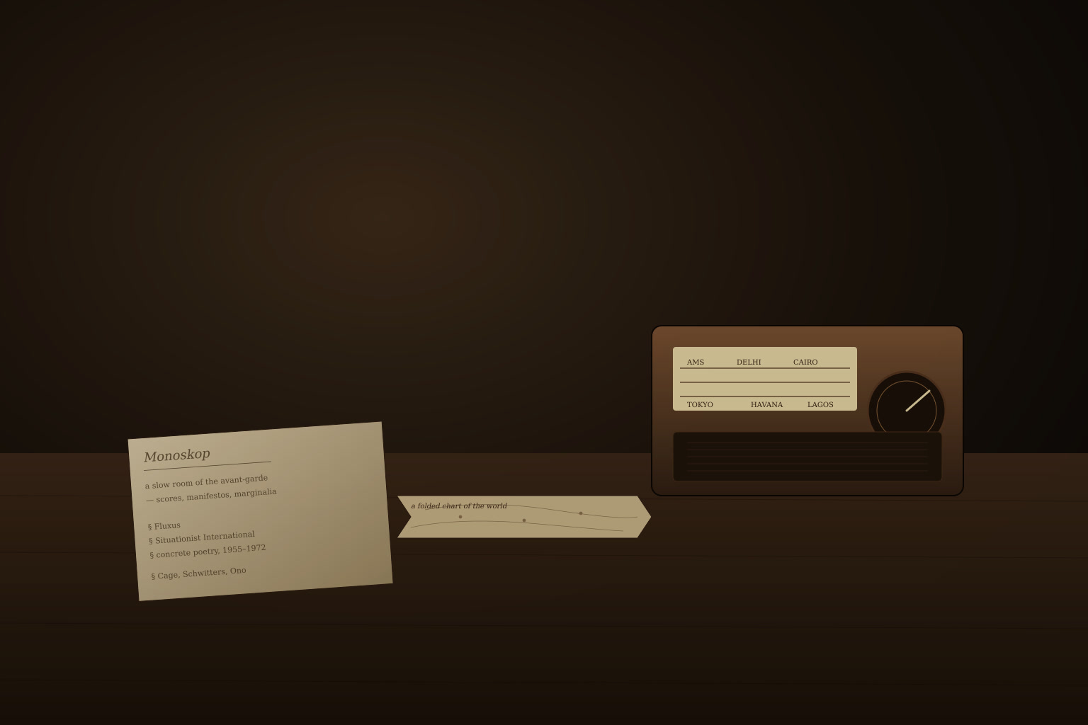 A quiet editorial vignette: a bakelite radio dial, a stack of pamphlets titled Monoskop, and a folded chart on a dark wooden table.