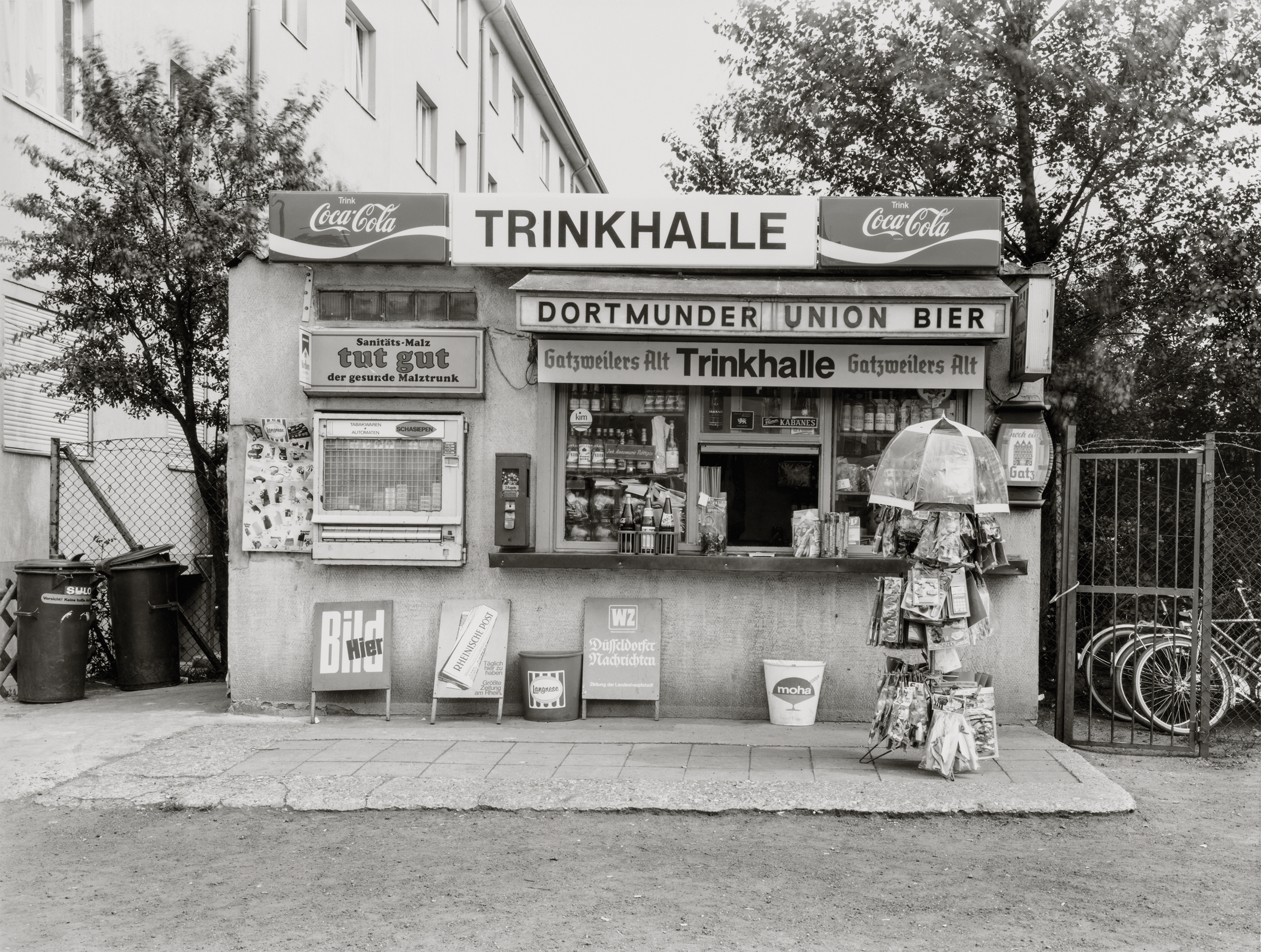 A photograph by Tata Ronkholz of a small German kiosk storefront, frontal and plain, full of commercial lettering and ordinary urban dignity.