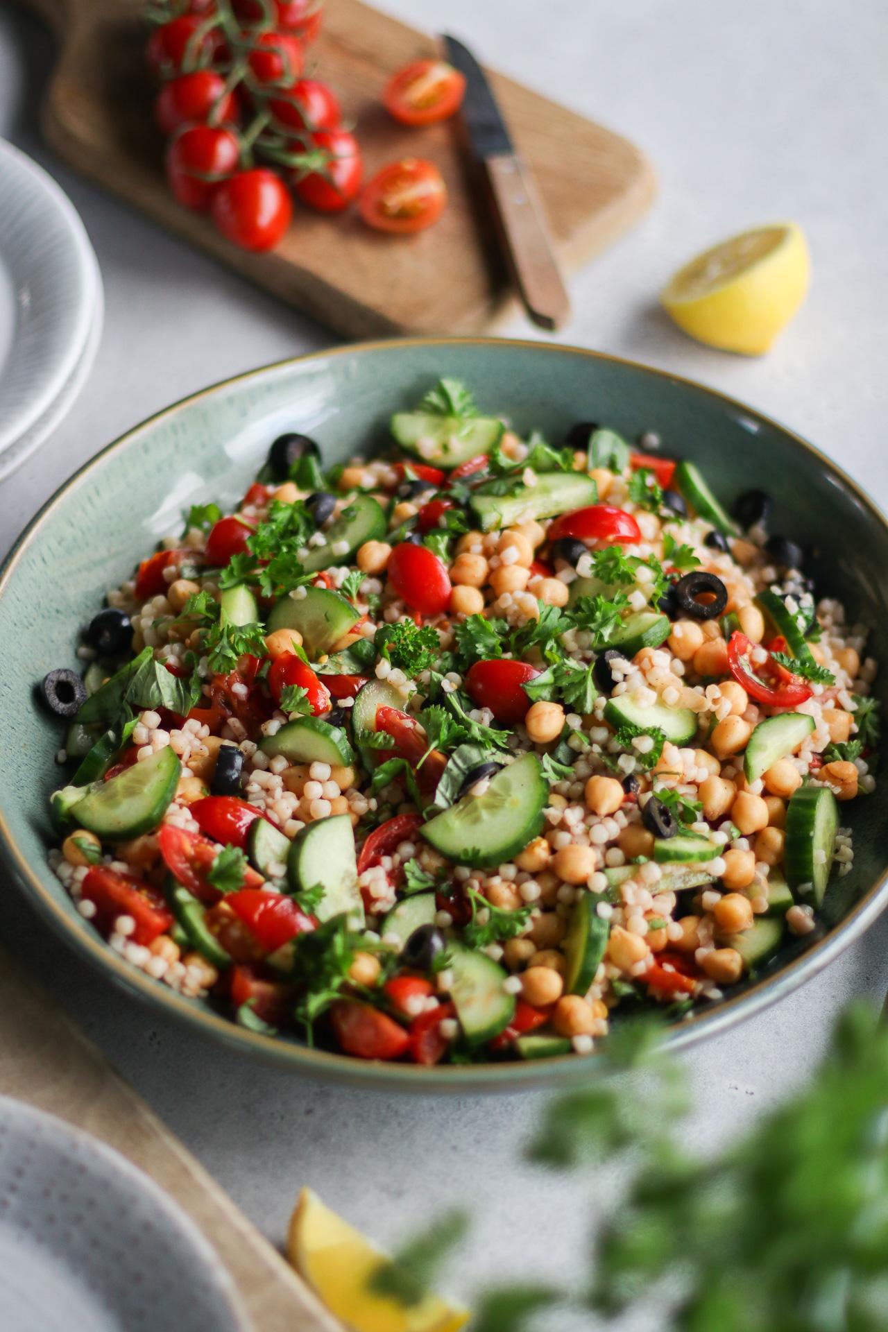 Warmer Perlcouscous-Salat mit Kichererbsen, Kirschtomaten, Oliven und frischen Kräutern.