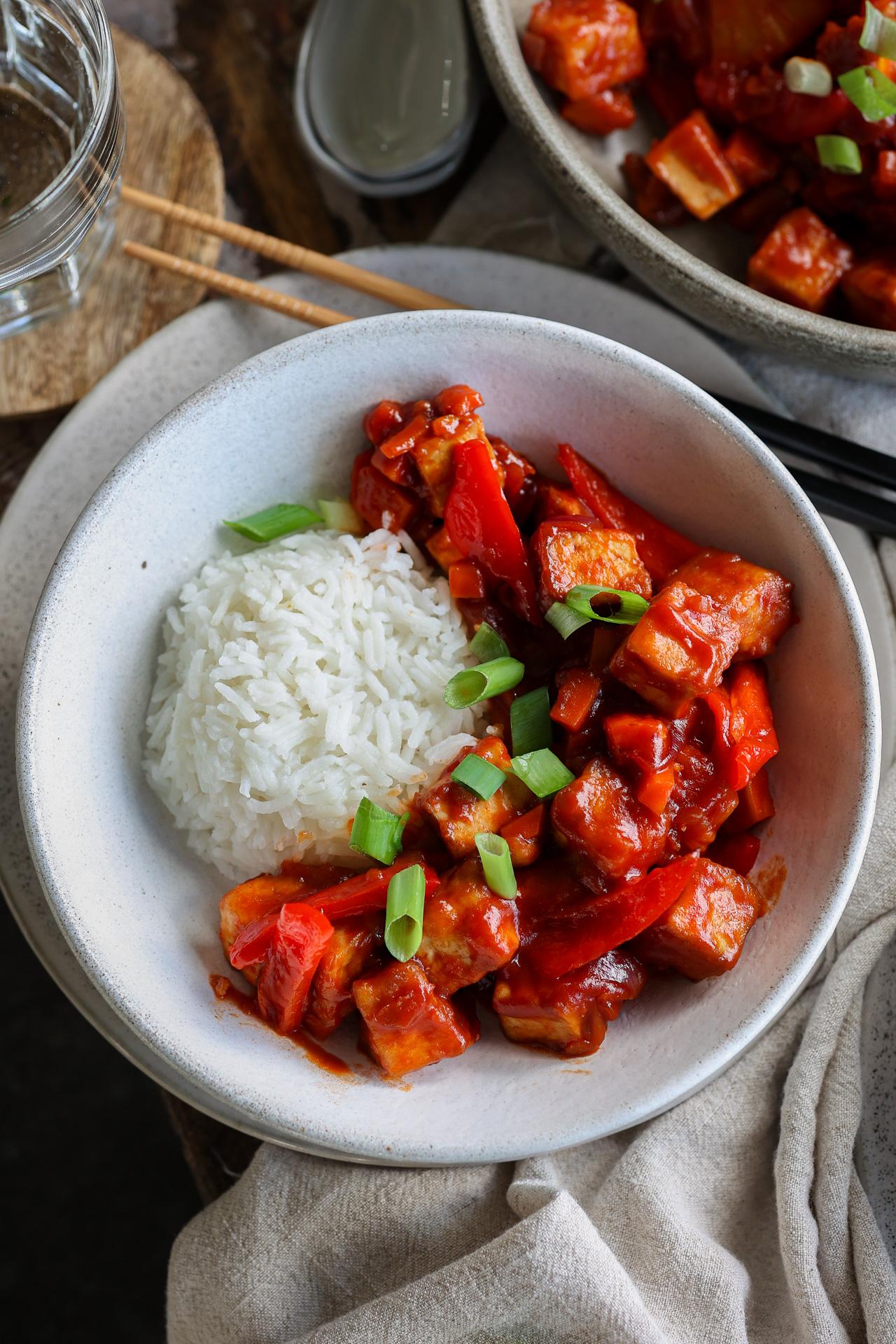 Süß-saure Tofu-Wokpfanne mit Paprika, roter Zwiebel und Ananas auf Reis.