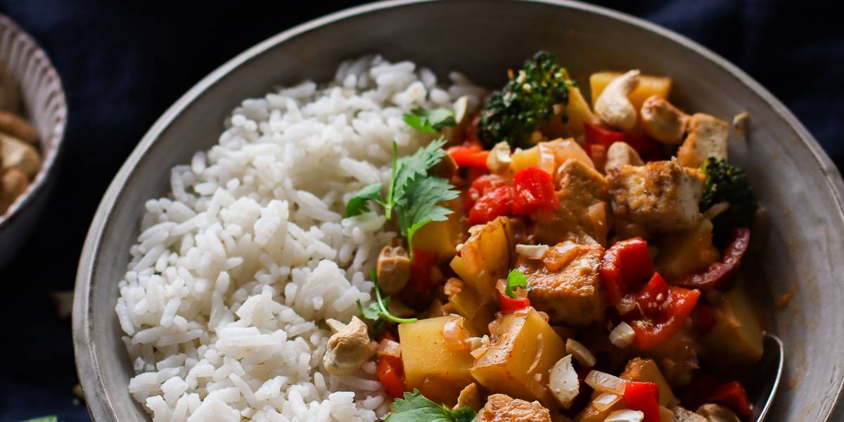 Red Thai coconut curry with tofu and summer vegetables in a dark bowl.