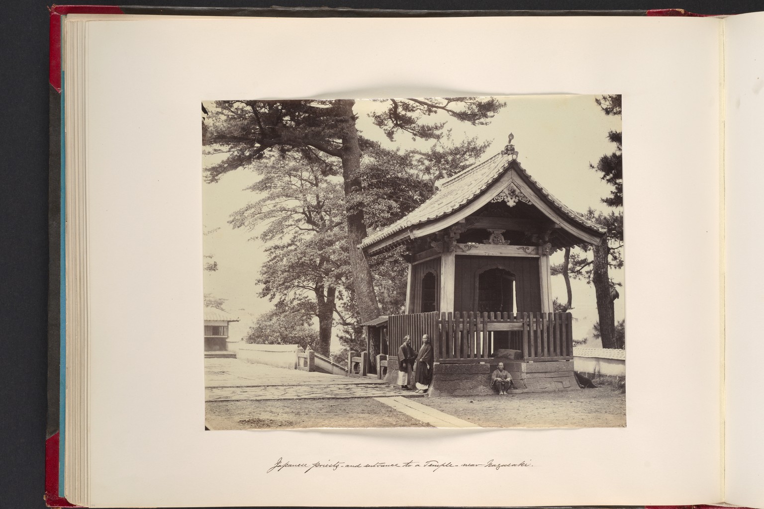 John Thomson's nineteenth-century photograph of Japanese priests at a temple entrance near Nagasaki, gathered at a deep threshold beneath a timbered roof.