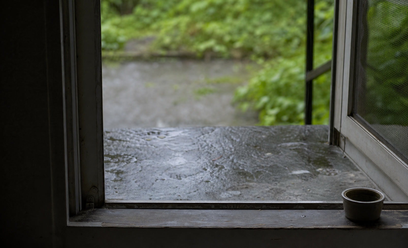 A rain-cleared room with an open window, pale grey light, and a wooden table returned to order.