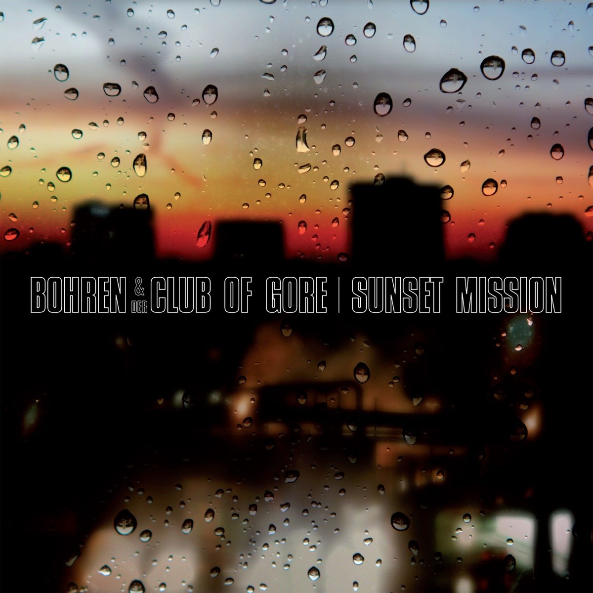 Original cover of Bohren & der Club of Gore's Sunset Mission (Wonder, 2000): a Ruhr city skyline silhouetted against a red-orange sunset, seen through a rain-spattered window.